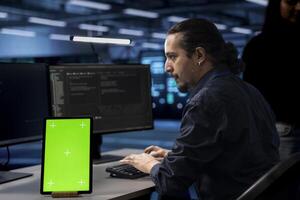 Technician in server hub using green screen tablet to repair equipment storing datasets. IT specialist using mockup device to do debugging on rigs doing computational operations photo