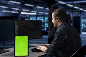 Engineer in server hub ensuring data remains shielded from potential threats using isolated screen tablet. Worker safeguarding data center hardware against malicious access with chroma key device photo