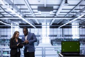 Focus on isolated screen laptop device used by coworkers in data center blurry background. Close up of Chroma key notebook in server hub optimizing data center infrastructure photo