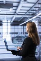 Software developer walking between server rows in data center, doing yearly infrastructure inspection. Worker in server farm establishment monitoring supercomputers equipment with laptop photo