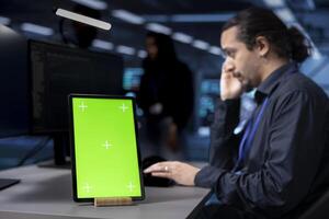 Focus on isolated screen tablet used by developer in blurry background to oversee servers used for managing databases. Close up shot of chroma key device used by IT expert in data center facility photo