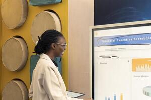African american employee creating a presentation with data reports and other statistics to help her colleagues with project insight. Providing initiatives to enhance operational efficiency. photo