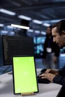 Focus on green screen tablet used by admin in blurry background to do maintenance in server farm. Close up shot of mockup device used by worker to monitor data center facility workplace photo