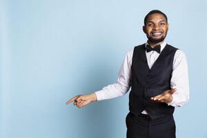 Doorman staff pointing at something to left or right sides in studio, indicating the direction for some amenities at the five star hotel. Bellboy porter wearing a suit and tie uniform on duty. photo