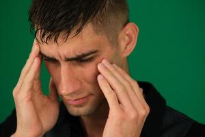 Unhealthy man suffering from migraines or dizziness sits on the couch at home, feels pain in his head. He is stressed, experiencing vertigo or headache, worrying about work or relationship problems. photo