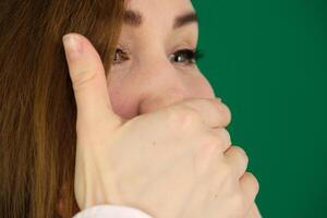 Surprised caucasian girl covering her mouth and looking at camera isolated over green background photo