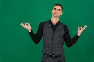 young businessman feeling successful and satisfied, smiling with mouth wide open, making okay sign with hand against green background photo