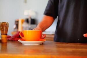 Carefully and intentionally placing a vibrant orange cup on a wooden table photo