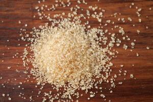 This image features a closeup view of a pile of brown sugar resting on a wooden surface photo