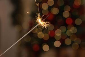 Burning sparkler in female hand on background of christmas tree lights in dark room photo