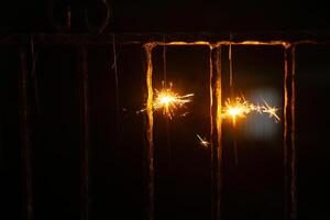 Two firework sparkles are hanging on fence in night with blurry background for new year event photo