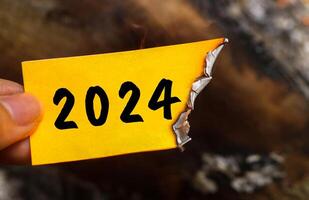 Hand holding a half-burnt note with 2024 written on it. new life and new year 2025 concept. 2024 paper is burning, say goodbye to 2024 photo
