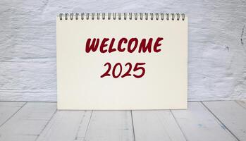 Welcome to 2025 message written on notebook with wall background. Conceptual welcome to 2025 symbol. Copy space. photo