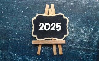 A small wooden-framed blackboard with 2025 written in white text on it. The blackboard with the concept of the new year 2025 on a wooden table. photo