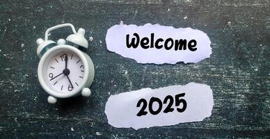 A scrap of paper with the words welcome 2025 surrounded by a clock on the table. New Year 2025 concept, welcoming the new year 2025 photo