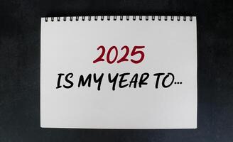 2025 is my year to be on notebook with white desk background. New year concept with typographic 2025 on notebook. Motivational words for the new year 2025 photo