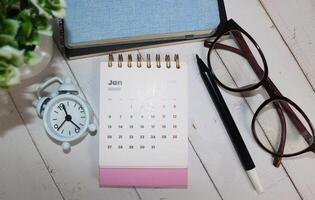 The first month of January 2025 in the pink 2025 calendar on the office desk with notebook, glasses and alarm clock. New year 2025 with office desk concept photo