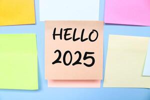 Hello 2025 written on sticky note attached to the wall isolated on blue background. New year concept with typographic 2025. Motivational words to welcome the new year 2025 photo