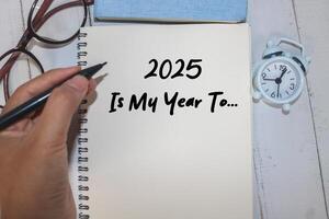 Hand writing 2025 is my year to on notebook with white desk background. New year concept with typographic 2025 on paper. Motivational words for the new year 2025 photo