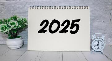 A workspace featuring a notepad with 2025 happy new year. Notebook on the table with the year 2025 written on it. photo