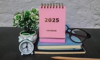Pink calendar 2025 on office desk with notebook, glasses, pen and alarm clock. New year 2025 with office desk concept photo