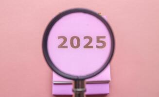 Magnifying glass in 2025 Calendar in pink isolated on pink background. Calendar and Note Pad Happy New year 2025. 2025 New Year resolutions goal, plan, and action concept photo