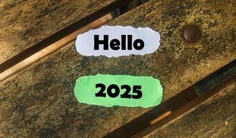 Hello 2025 on torn paper on wooden table. New year concept with typographic Hello 2025 on paper. photo