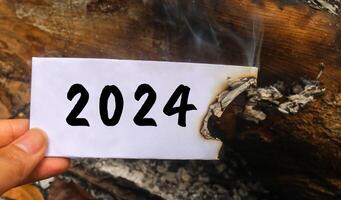 Hand holding a half-burnt note with 2024 written on it. new life and new year 2025 concept. 2024 paper is burning, say goodbye to 2024 photo