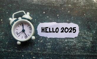 A paper cutout with Hello 2025 written on it is surrounded by a clock on the table. New Year 2025 concept, welcoming the new year 2025 photo