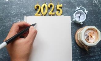 candles in shape of 2025 year on blank notebook, hand writing notes on blank paper, blank space for text. New Year 2025 celebration. photo