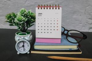 The first month of January 2025 in the pink 2025 calendar on the office desk with a notebook and alarm clock. New year 2025 with office desk concept photo