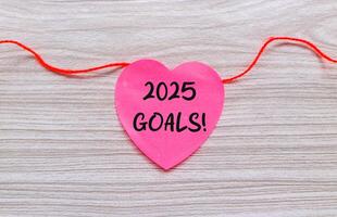 2025 Goals notes on pink heart shaped paper hanging on a string. New year concept with typographic 2025. Motivational words for the new year 2025 photo