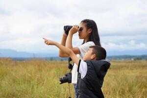 Children use binoculars to look at nature, birds, animals in the field during family camping on vacation. with the concept of learning outside the classroom nature study, exploration. photo