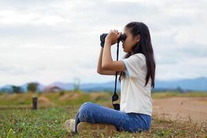 Asian girl uses binoculars to explore nature in the field. the concept of learning outside the classroom nature study, exploration. photo