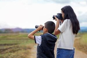 A boy uses binoculars and a girl uses a digital camera to explore nature in a field. Concept of exploration, outside the classroom, outdoors, ecology, nature, learning, travel. photo