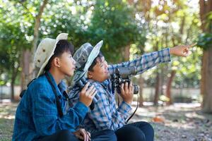 Two Asian boys use binoculars to study the local birds in a community forest. Soft and selective focus. photo