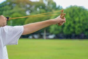 Hand holding Slingshot on green background It is a weapon made from a forked stick with rubber attached to a leather strip that holds bullets to be fired. photo