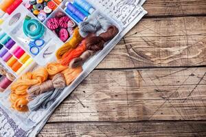Floss threads and colored thin threads on a spool. Buttons and scissors are in the box. A wooden table. Copy space photo