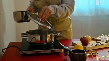 Person preparing mulled wine in a kitchen with fruits and spices photo