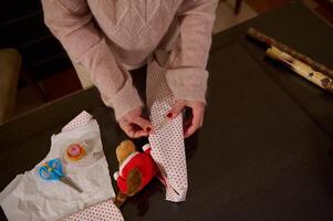 Wrapping a toy teddy in festive paper on a wooden table photo