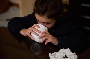 Young girl drinking from white cup while sitting indoors in dim lighting photo