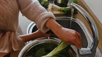 Person washing vegetables under running water in a kitchen sink photo