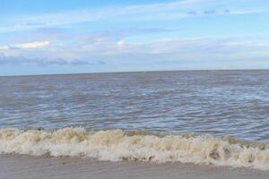 Gentle Waves on a Calm Sea. Gentle waves lapping a sandy beach under a partly cloudy sky. photo