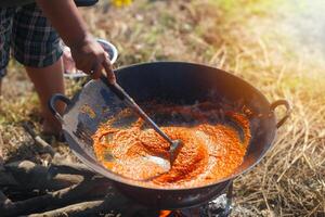 Outdoor Spicy Stir-Fry in Progress. A person stirs a curry seasoning simmering in a large wok over an open fire. photo
