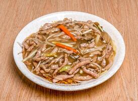 Stir fried egg noodles with shredded pork served in plate dish isolated on wooden table side view of hong kong food photo