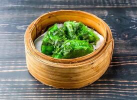 Coriander Miao Dumplings served in bamboo steamer isolated on wooden table side view of hong kong food photo