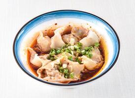 Spicy Wonton Soup in red oil with scallions served in bowl isolated on white background side view of hong kong food photo