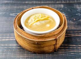 Clear soup dumplings served in pot on bamboo steamer isolated on wooden table side view of hong kong food photo