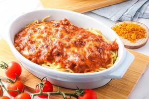 Baked Spaghetti with Sausage and Cheese with Bolognese Sauce topped with a layer of melted cheese served in dish isolated on wooden board closeup side view of italian food photo