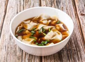 Wonton Soup with Green Onions served in bowl isolated on wooden table side view of hong kong food photo